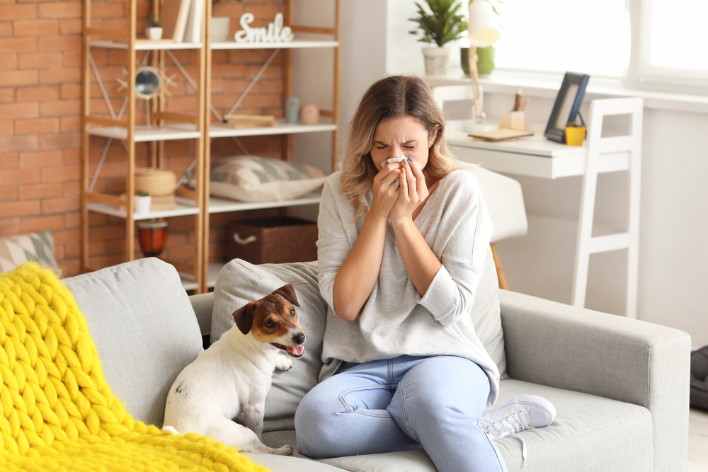 woman blowing nose on couch next to dog