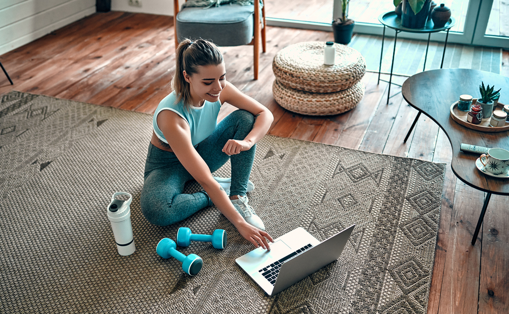 woman looking up workout ideas on floor next to weights and water bottle