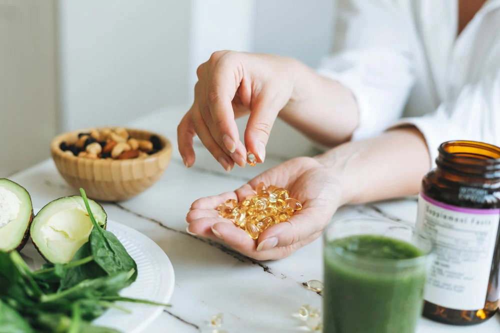 woman with handful of pills surrounded by green smoothie, salad, and nuts